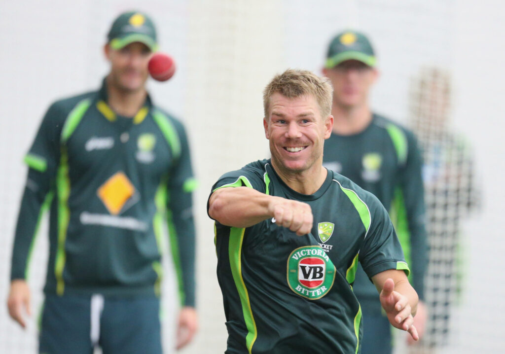 David Warner in green Australian cricket uniform throwing ball during energetic practice session Wallpaper