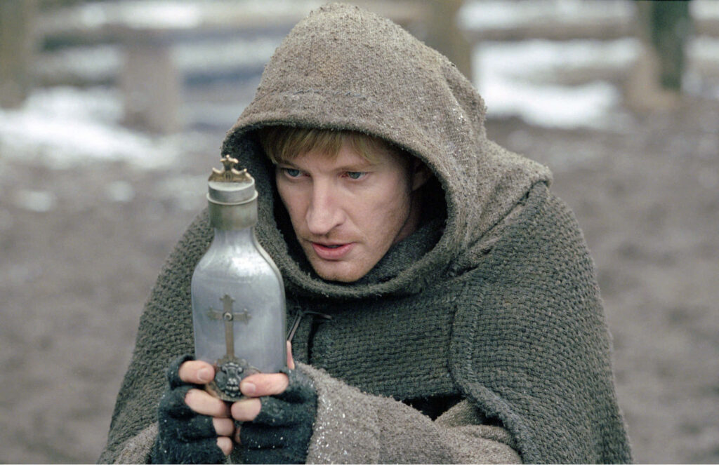 David Wenham in medieval chainmail and hooded cloak holding glass cross relic in wintry scene Wallpaper