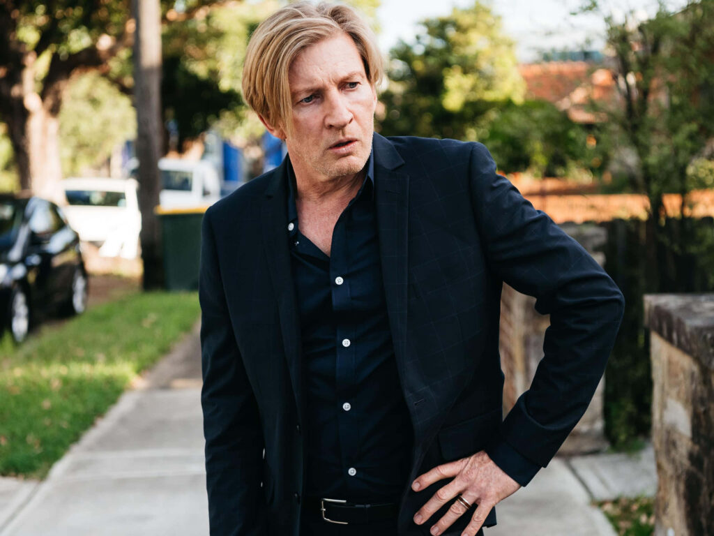 David Wenham in dark suit outdoors with vibrant greenery sunlight suburban background wallpaper