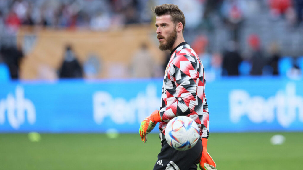 David de Gea in vibrant geometric goalkeeper jersey with orange gloves holding football on pitch Wallpaper