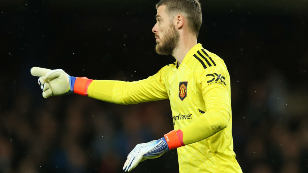 David de Gea in bright yellow Manchester United goalkeeper kit directing teammates on pitch under stadium lights Wallpaper