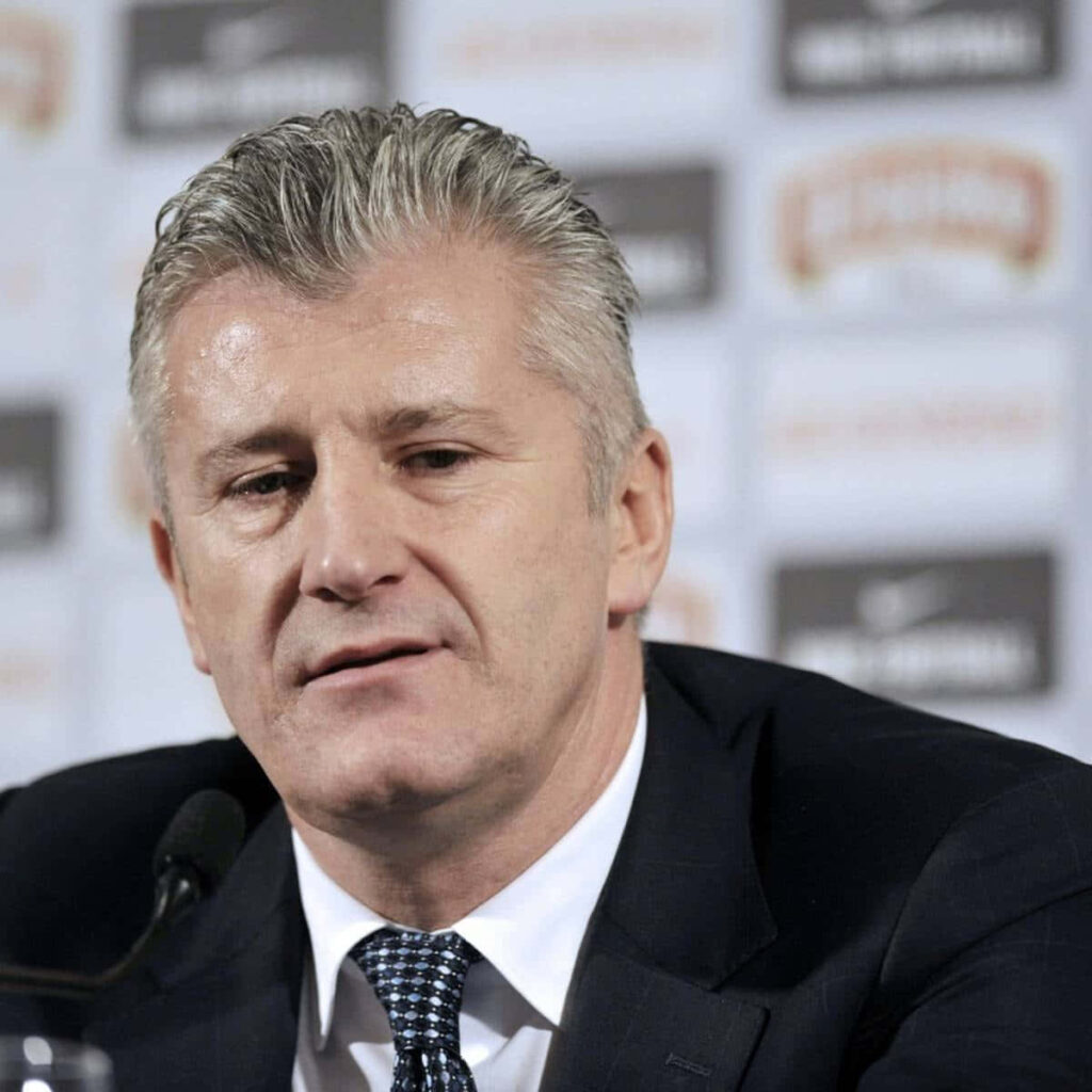 Davor Šuker at football press conference in dark suit patterned tie professional branded backdrop Wallpaper