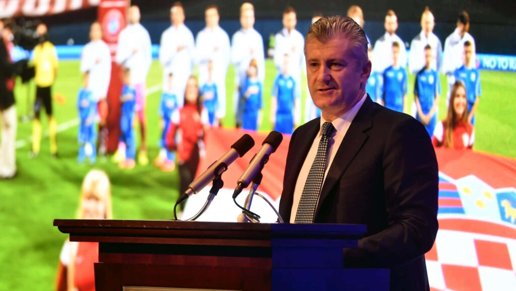 Davor Šuker delivering speech at podium with Croatian flag football field background wallpaper
