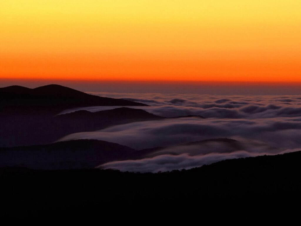 Dawn mountain wallpaper with layered peaks above clouds glowing orange serene high altitude view