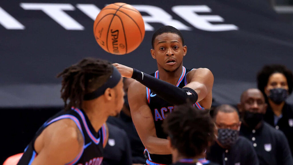De'Aaron Fox basketball pass NBA game intense action athletic focus dynamic court backdrop Wallpaper