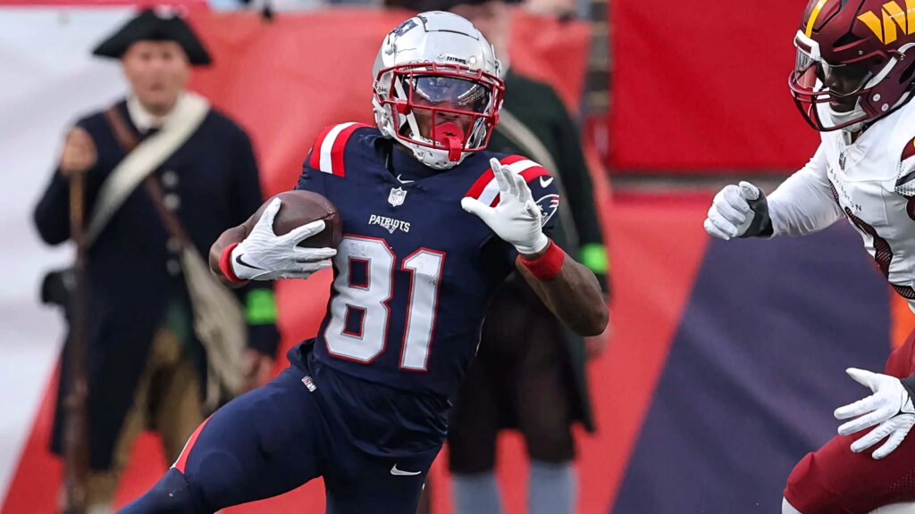 DeMario Douglas in Patriots uniform sprinting on field evading tackle during football game action Wallpaper