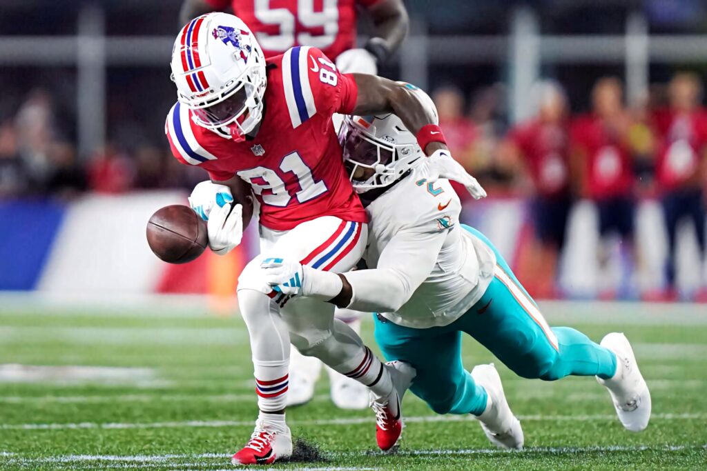 DeMario Douglas in Patriots gear evades Dolphins tackle under bright stadium lights football action Wallpaper