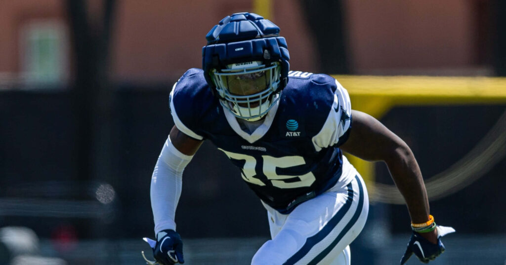 DeMarvion Overshown in football gear focused on action with blurred blue white field background Wallpaper