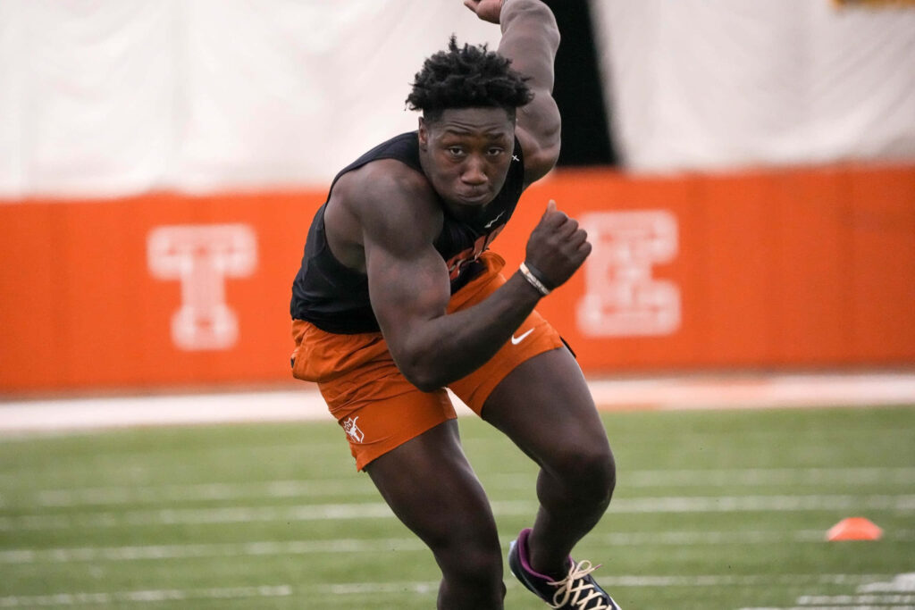 DeMarvion Overshown in mid-motion during intense football training drill on vibrant orange field Wallpaper