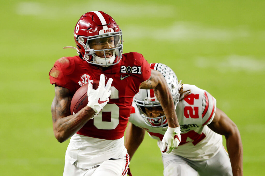 DeVonta Smith running with football in red and white uniform during intense college game action Wallpaper