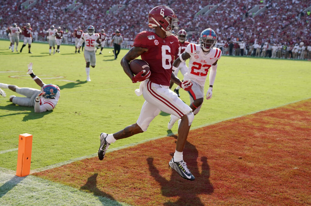 DeVonta Smith sprinting mid-stride for touchdown on green field with vibrant red end zone background Wallpaper