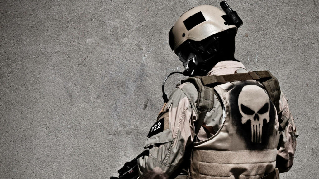 Soldier in tan combat gear with Punisher skull vest against gray concrete wall wallpaper