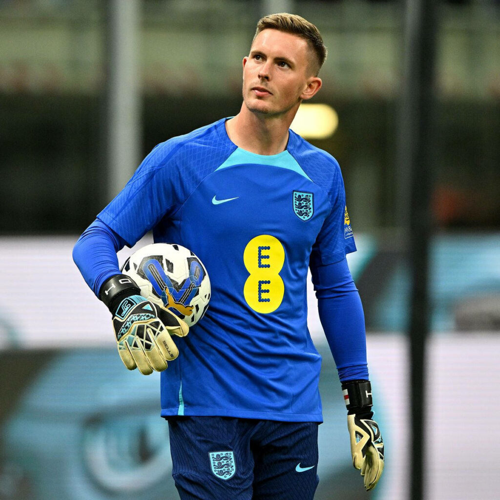 Dean Henderson in blue England goalkeeper kit holding white football focused in stadium portrait Wallpaper