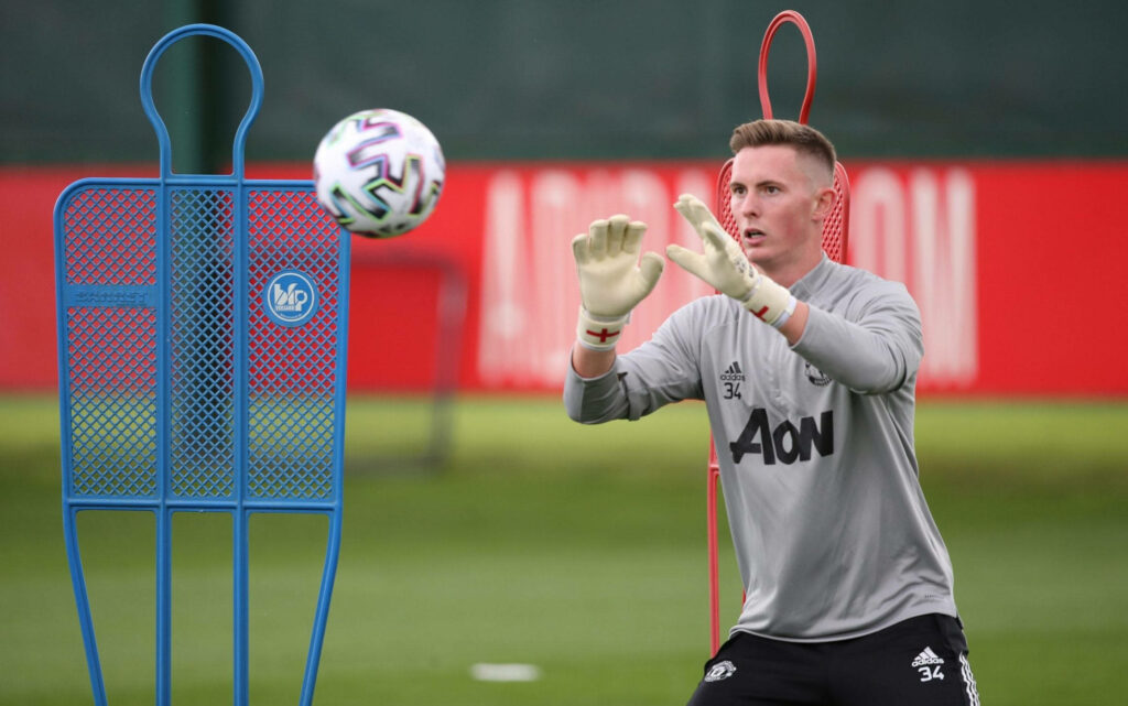 Dean Henderson catching football during intense training on vibrant green field with mannequins Wallpaper