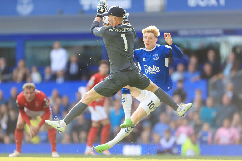 Dean Henderson mid-air making a dynamic jump catch as Anthony Gordon charges in intense football match Wallpaper