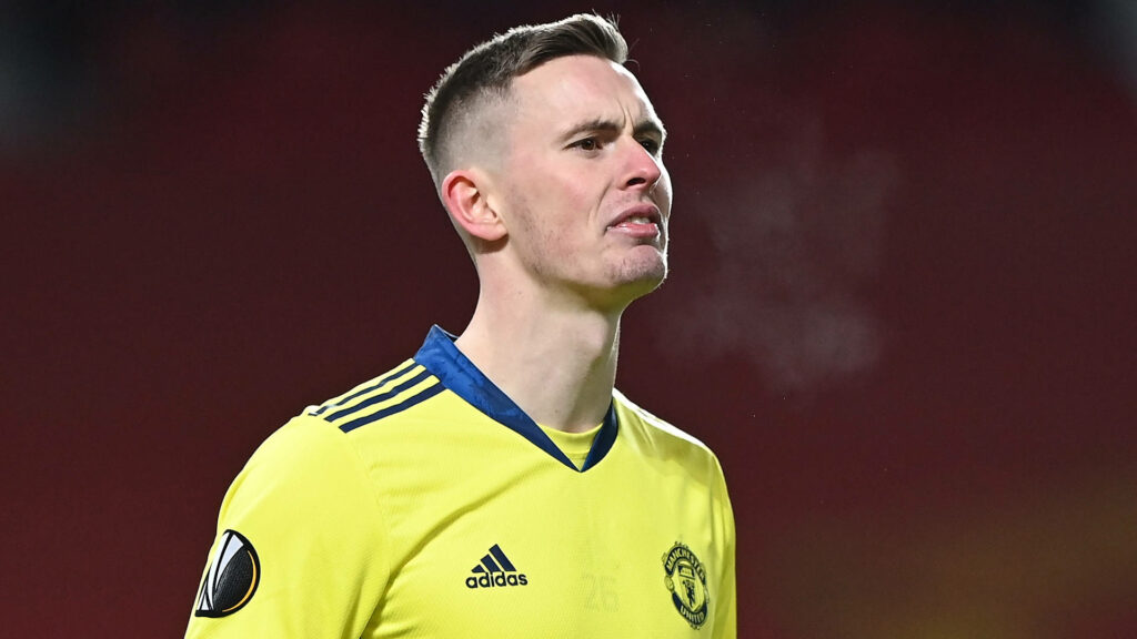 Dean Henderson intense focused frown Manchester United goalkeeper yellow jersey deep red background Wallpaper