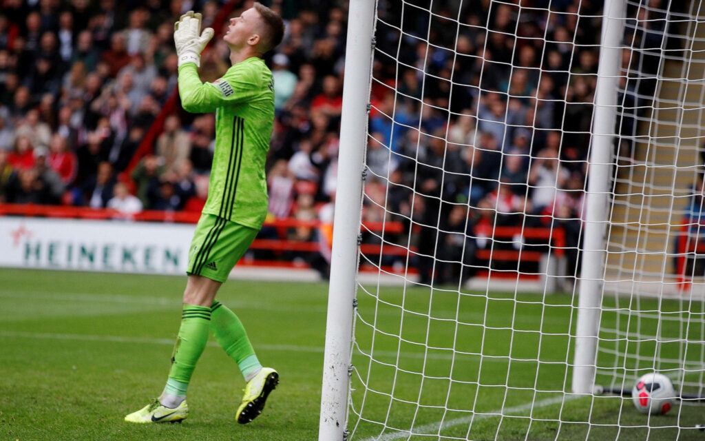 Dean Henderson in green goalkeeper kit raising gloves on football pitch by goalpost with crowd background Wallpaper