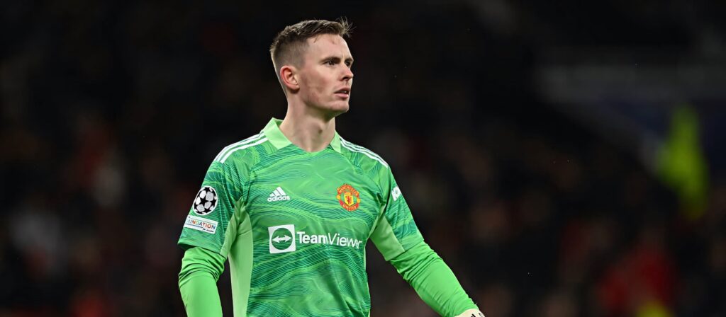 Dean Henderson in green Manchester United goalkeeper kit poised in dark stadium wallpaper background