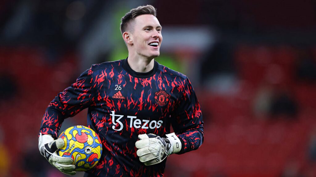 Dean Henderson running with ball in Manchester United red training kit on football pitch dynamic action Wallpaper