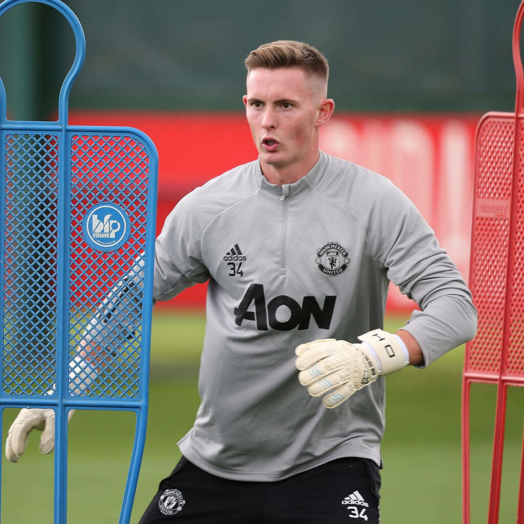 Dean Henderson in grey Manchester United kit training as goalkeeper with gloves on green field Wallpaper