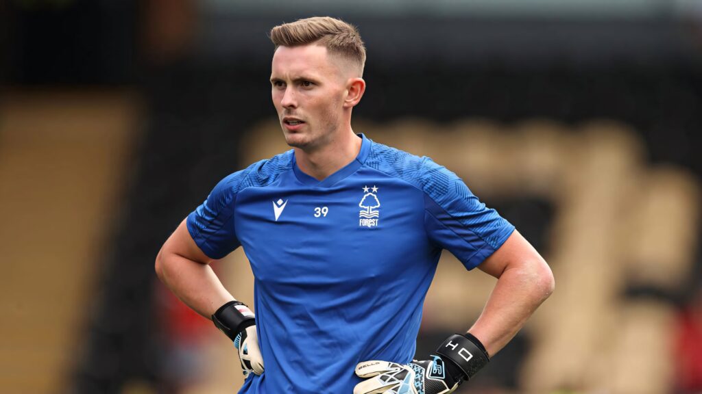 Dean Henderson in blue Nottingham Forest kit with goalkeeper gloves stands confident stadium backdrop Wallpaper