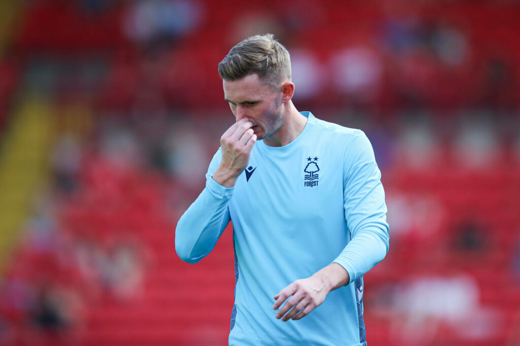 Dean Henderson in light blue Nottingham Forest training kit against blurred red stadium background Wallpaper