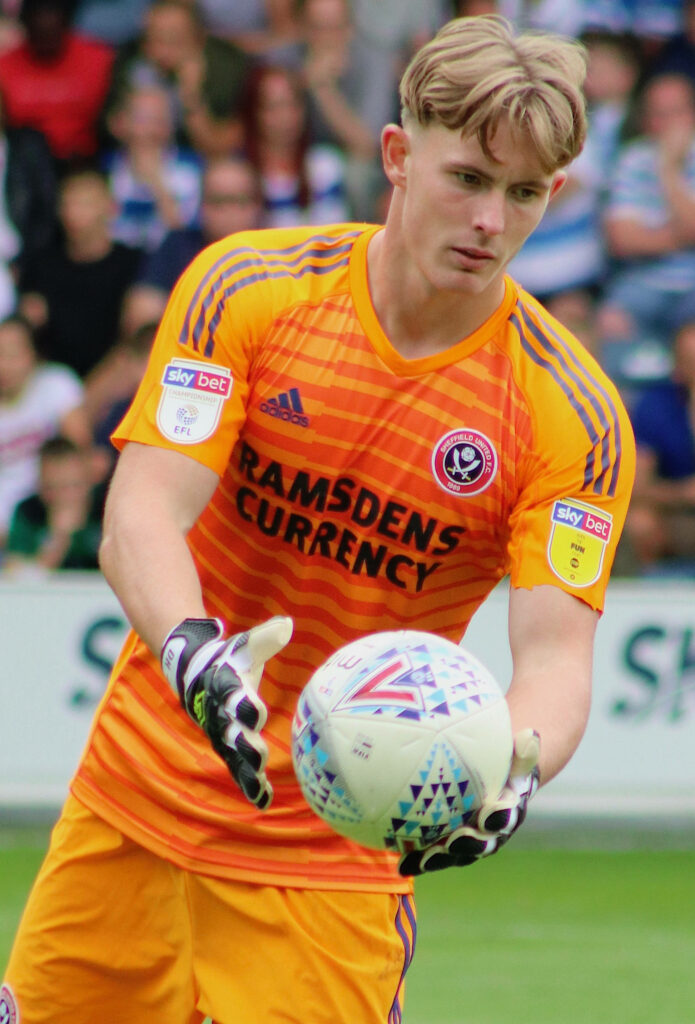 Dean Henderson in orange Sheffield United goalkeeper kit catching ball focused in match action Wallpaper