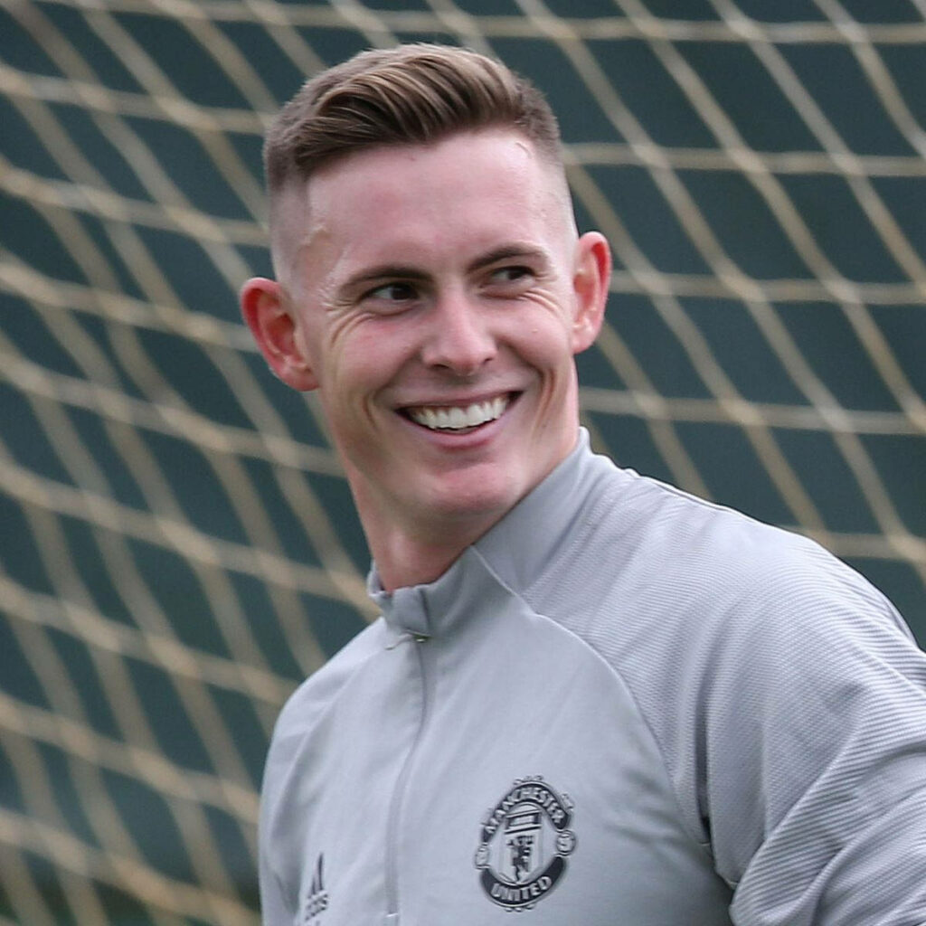 Dean Henderson smiling in light gray Manchester United training top with blurred football net background Wallpaper