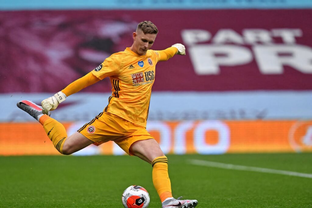 Dean Henderson in bright yellow goalkeeper kit kicking football on green pitch during pro match Wallpaper