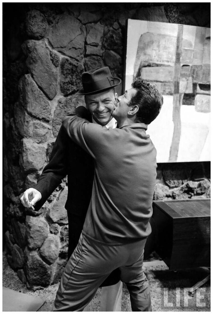 Dean Martin warmly hugging smiling man mid century modern stone wall retro Hollywood camaraderie Wallpaper