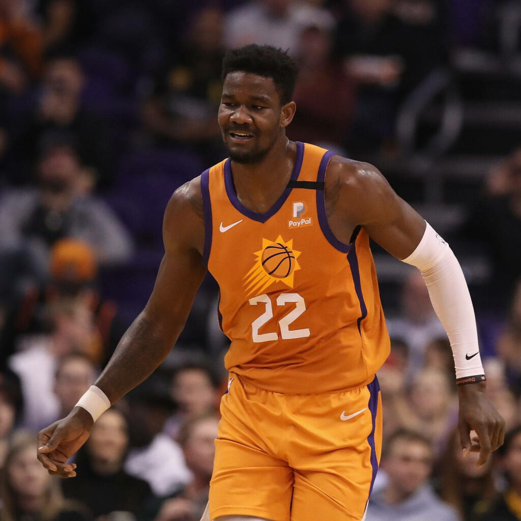 Deandre Ayton in Phoenix Suns orange jersey number 22 on court with cheering NBA fans background Wallpaper