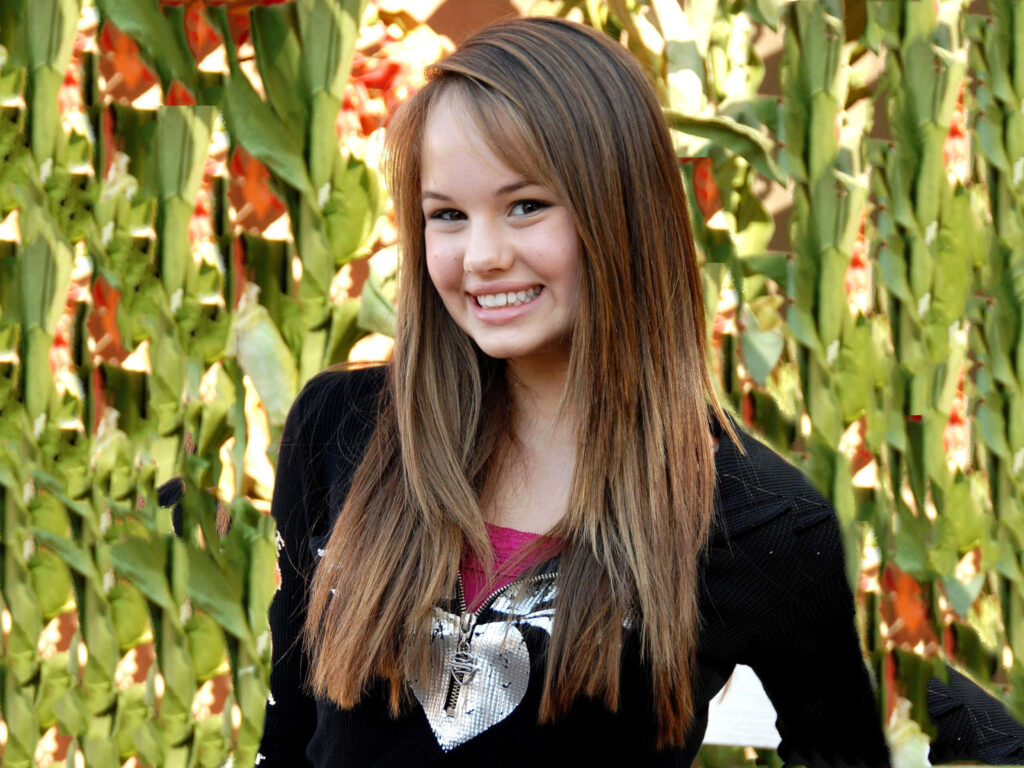Debby Ryan smiling outdoors with light brown hair black heart top green foliage background natural light Wallpaper