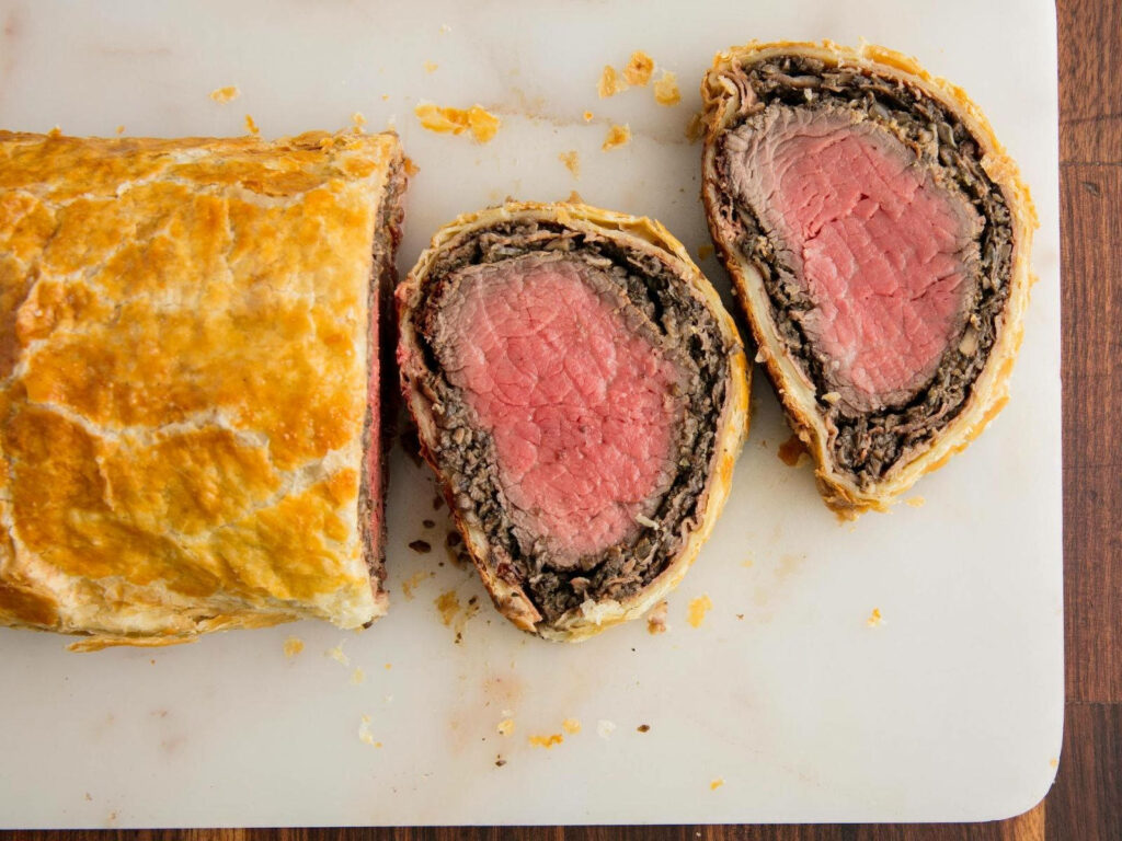 Beef Wellington with golden flaky crust and tender pink center on elegant wallpaper background