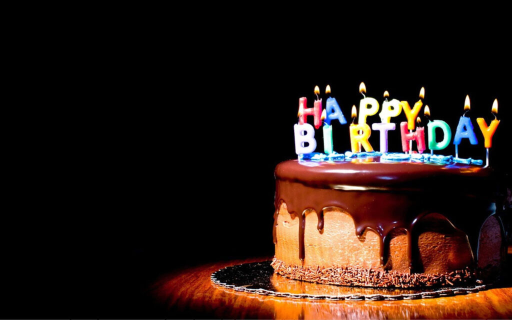 Decadent chocolate birthday cake with colorful candles and glossy ganache on wooden surface Wallpaper