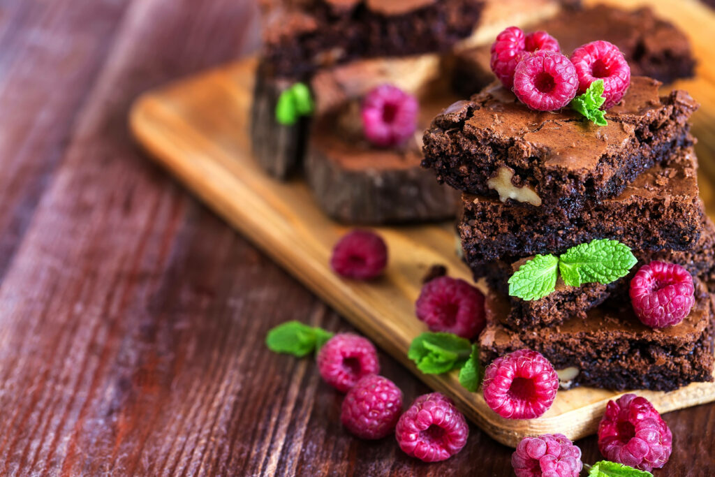 Stacked chocolate brownies with fresh raspberries and mint on a rustic wooden board background Wallpaper