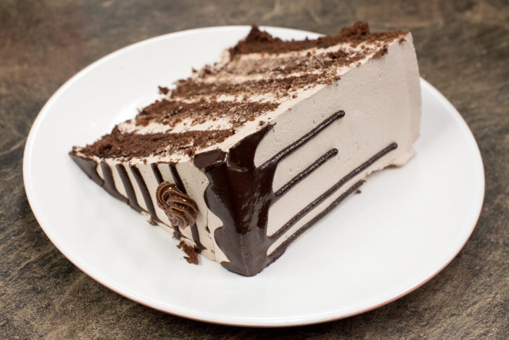 Indulgent Chocolate Cake Slice with Creamy Frosting on White Plate Wallpaper