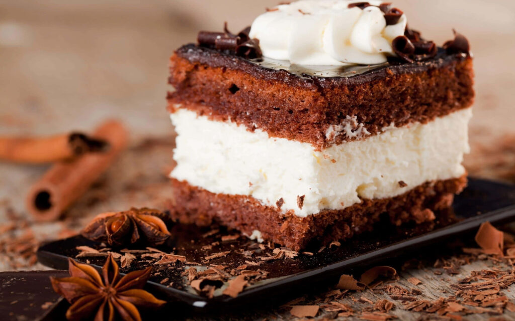 Slice of rich chocolate cake with creamy white frosting chocolate shavings on wooden background Wallpaper