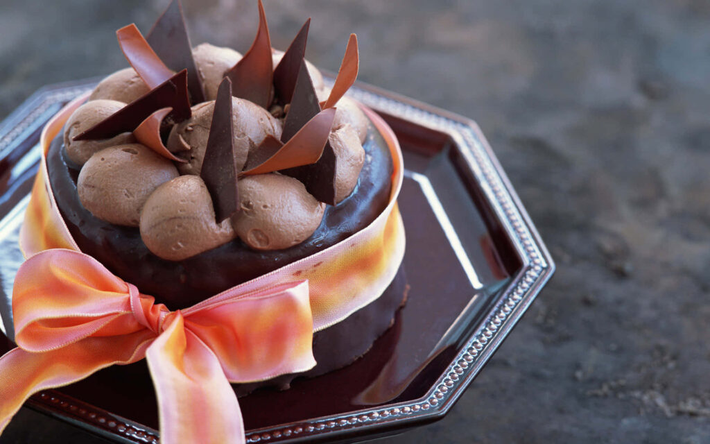 Decadent chocolate cake with creamy swirls and chocolate shards wrapped in satin ribbon wallpaper