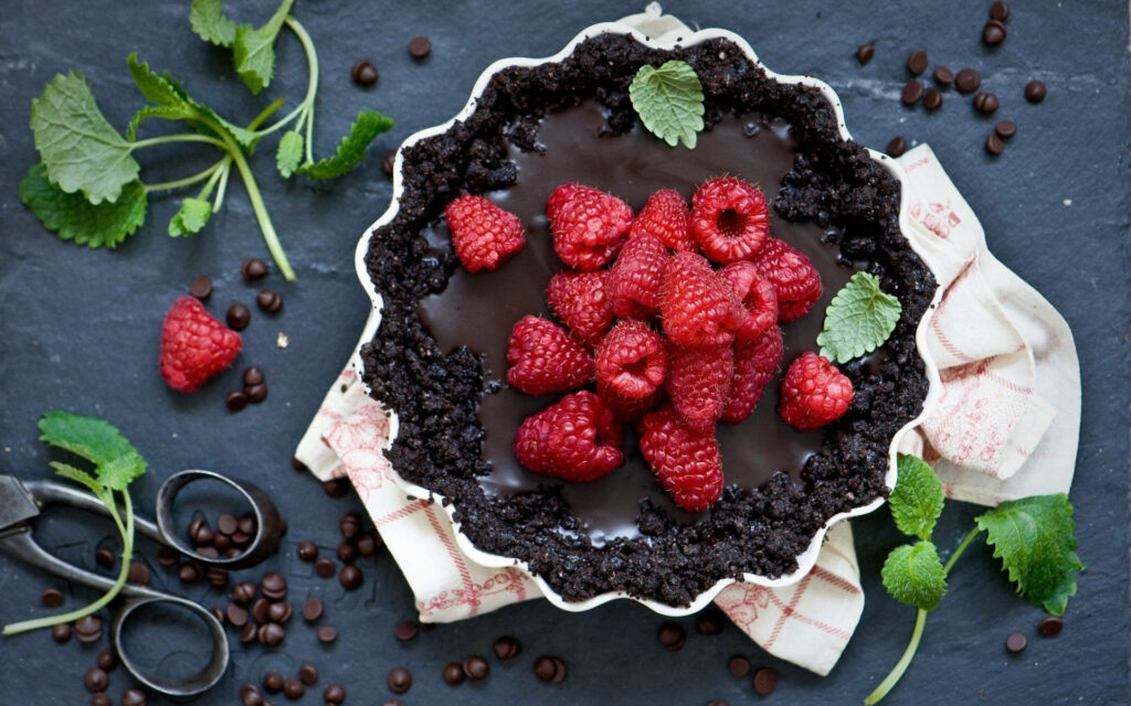 Decadent chocolate cake topped with fresh raspberries and mint leaves on rustic dark background Wallpaper