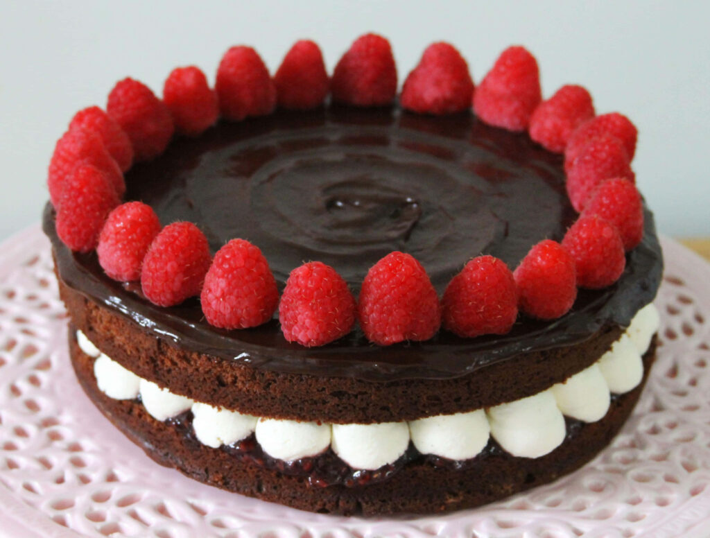 Dark chocolate cake with glossy ganache creamy filling fresh raspberries on pink lace plate Wallpaper