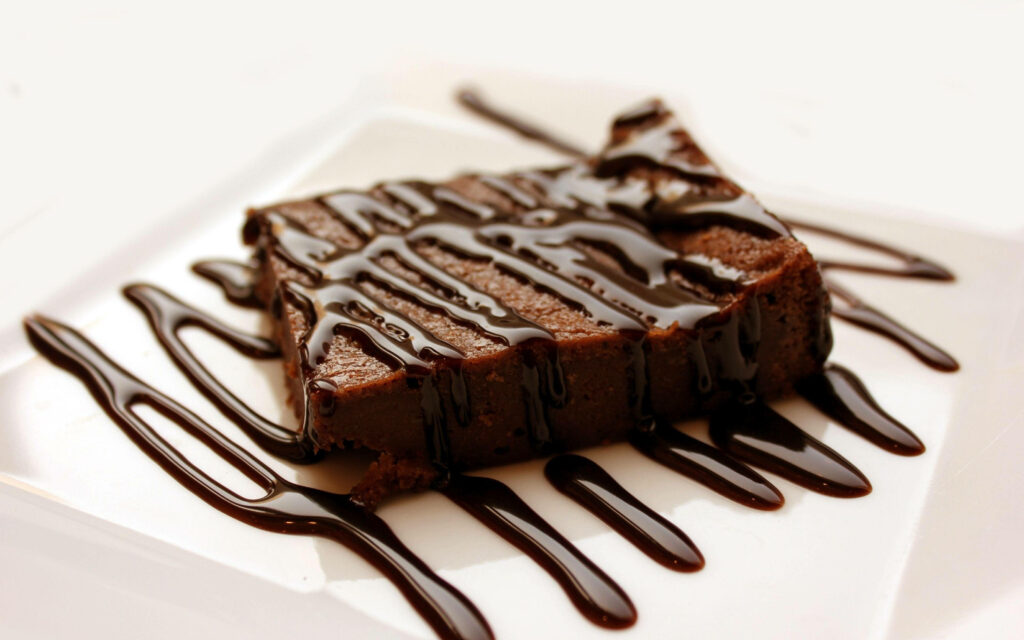 Decadent moist chocolate brownie with glossy chocolate drizzle on white plate dessert background Wallpaper