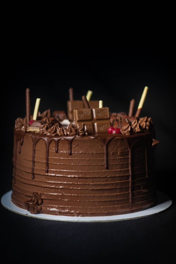 Rich multi-layered chocolate cake with Milka pieces cream swirls and red berries on black background Wallpaper