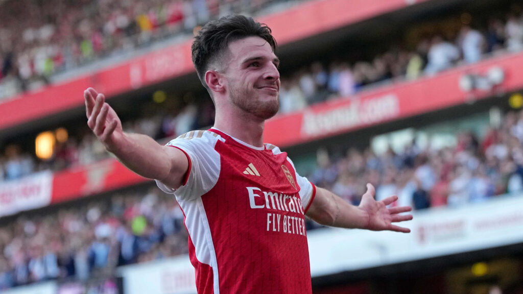 Declan Rice celebrates triumph in red and white Arsenal jersey with vibrant stadium background Wallpaper