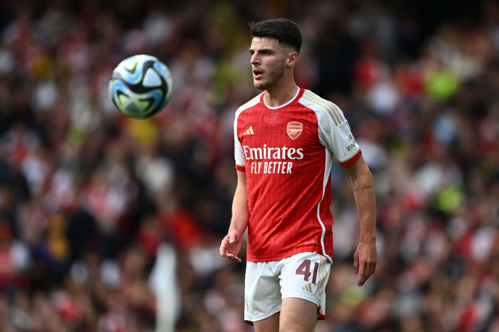 Declan Rice focused in Arsenal red and white kit during intense soccer match with blurred crowd background Wallpaper