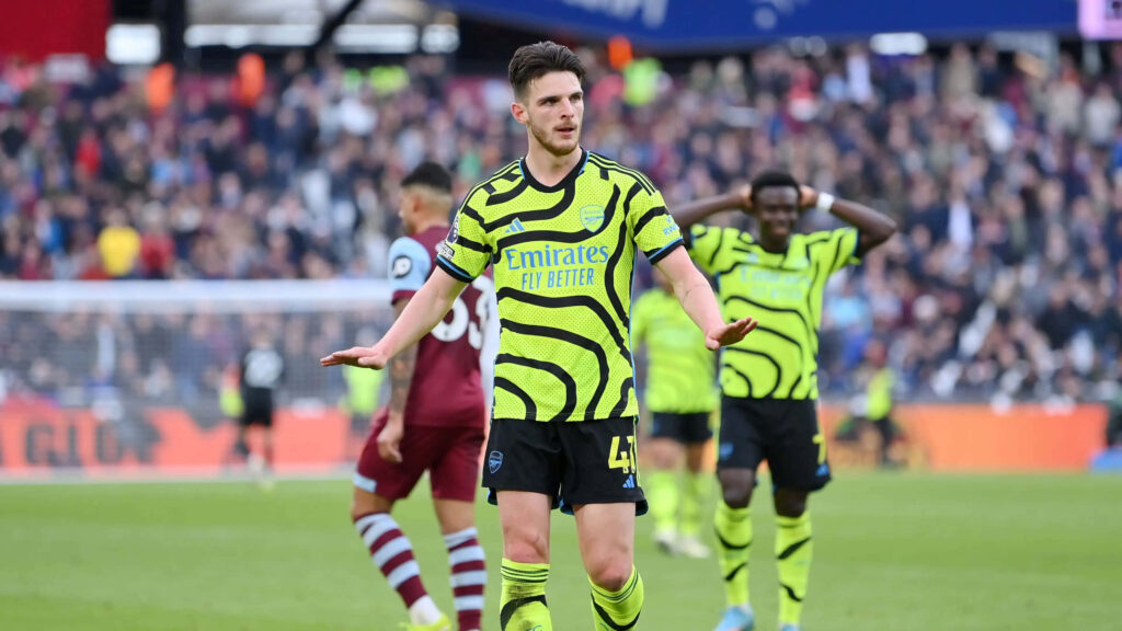 Declan Rice in Arsenal neon green away kit during intense football match with vibrant stadium crowd Wallpaper