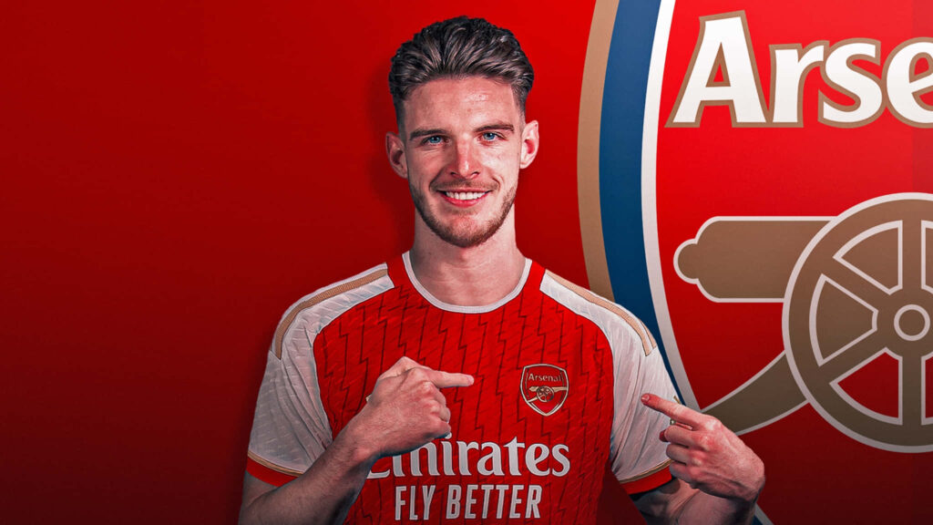Declan Rice in Arsenal kit pointing at club badge against red background with Arsenal logo Wallpaper