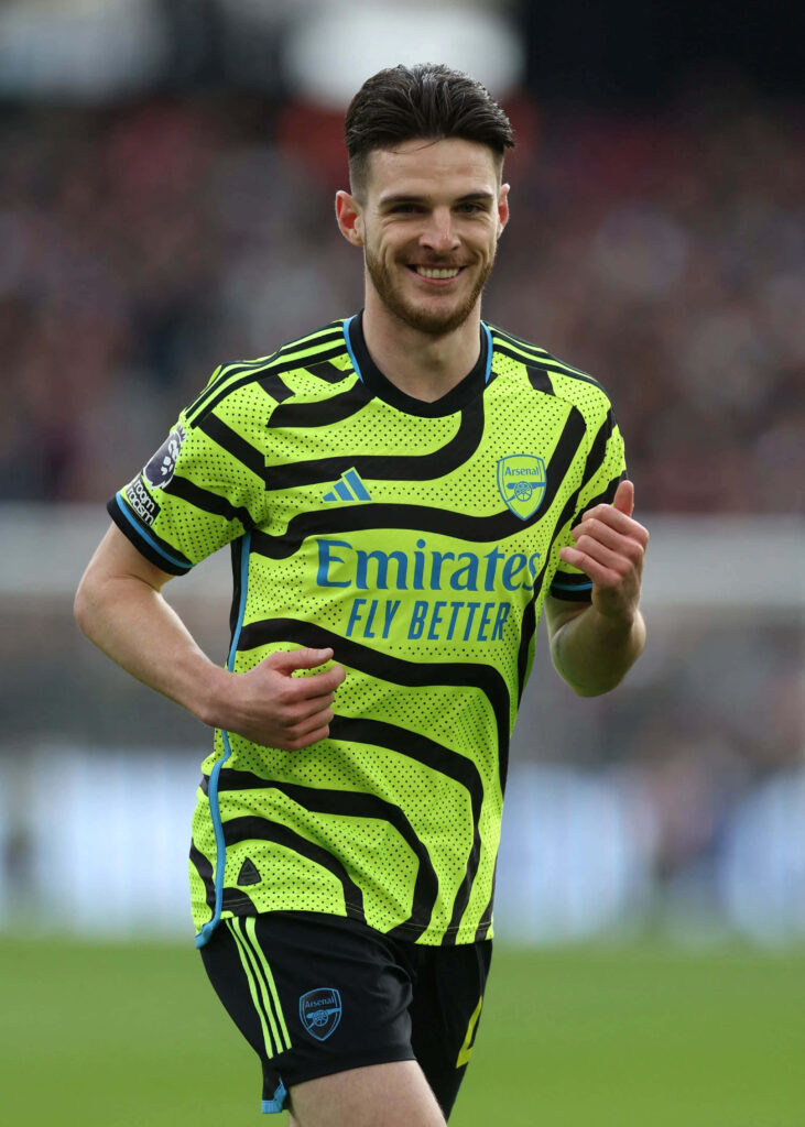 Declan Rice in neon green Arsenal away jersey smiling mid-game vibrant dynamic soccer action Wallpaper