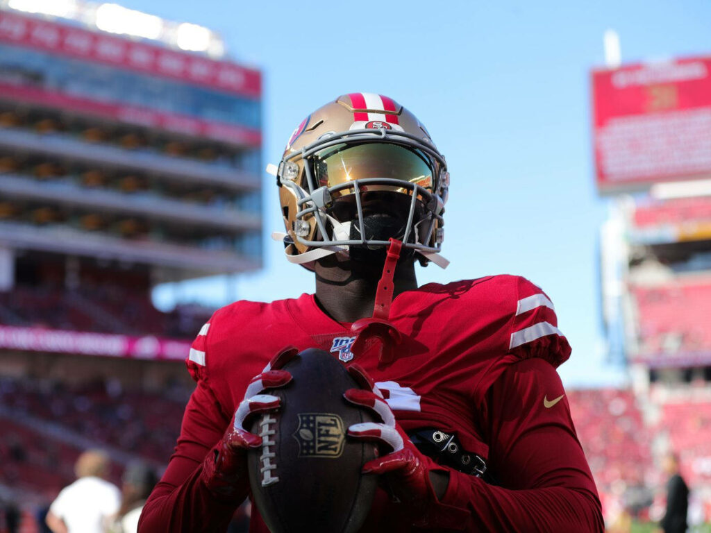 Deebo Samuel Sr in San Francisco 49ers uniform gripping football focused on game day field Wallpaper