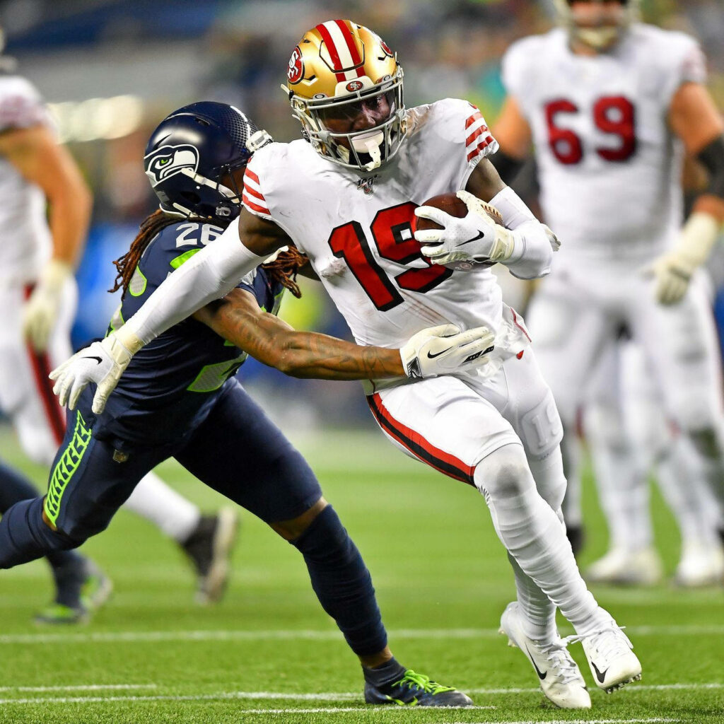 Deebo Samuel Sr in San Francisco 49ers uniform evading Seahawks defender on green football field Wallpaper