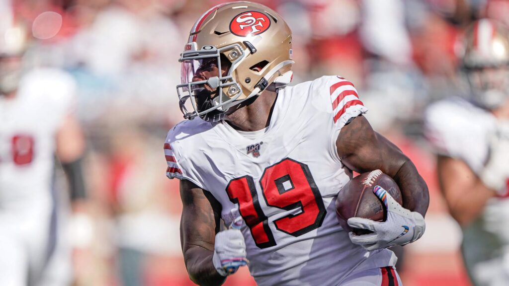 Deebo Samuel Sr in San Francisco 49ers uniform gripping football intense game action stadium Wallpaper
